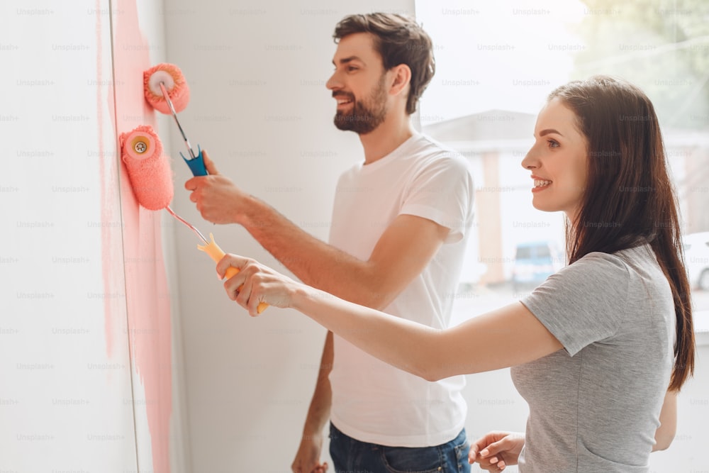 Homem e mulher jovens que fazem o reparo do apartamento juntos pintam as paredes