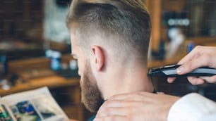 Hombre joven sentado en una barbería mientras el peluquero recorta el cabello