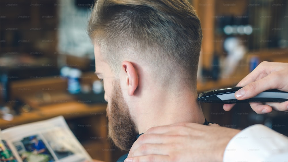 Young man sitting in a barbershop while barber trimming the hair