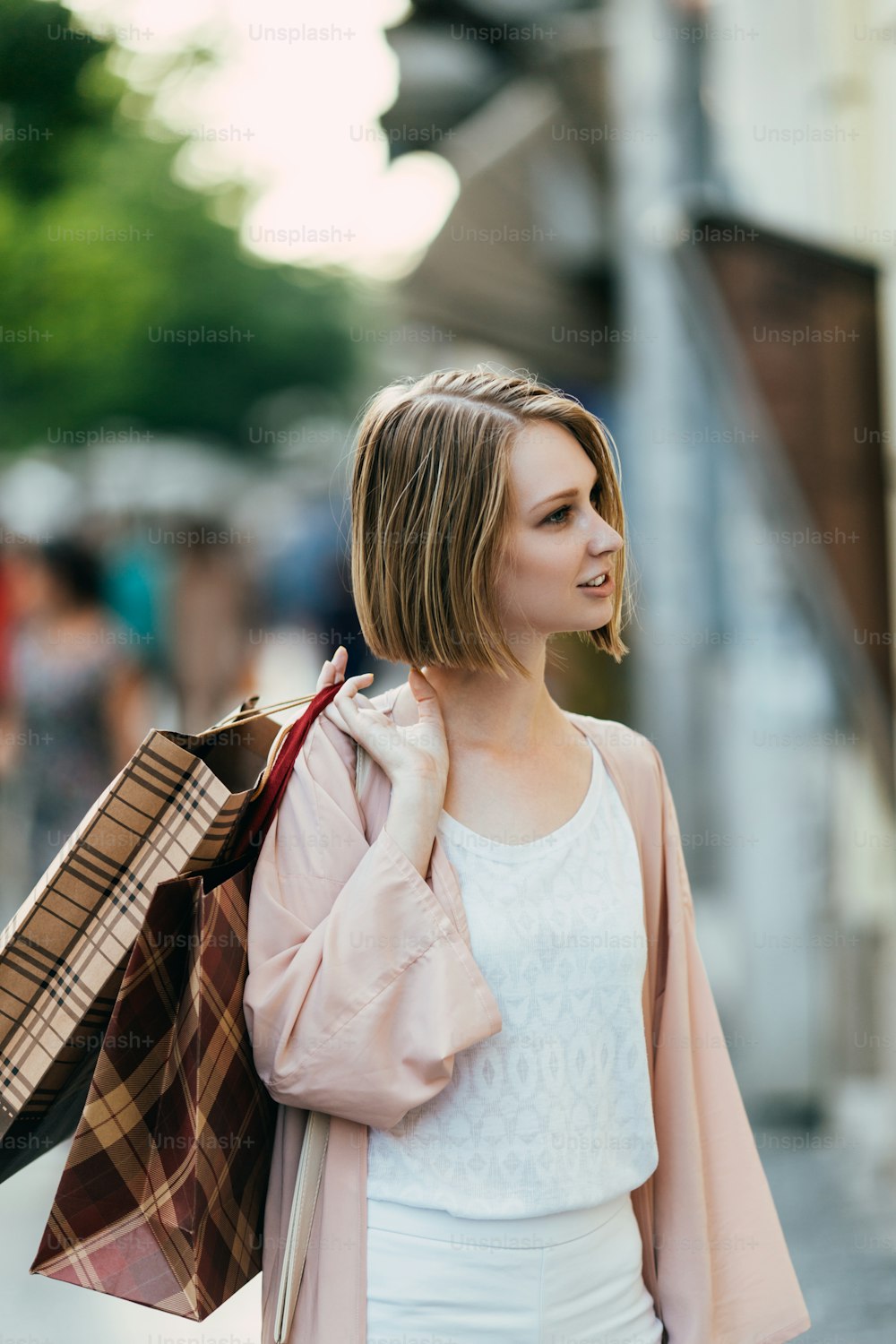 Schöne und modische junge Frau mit Einkaufstaschen, die auf der Stadtstraße steht und auf die Ladenfront schaut