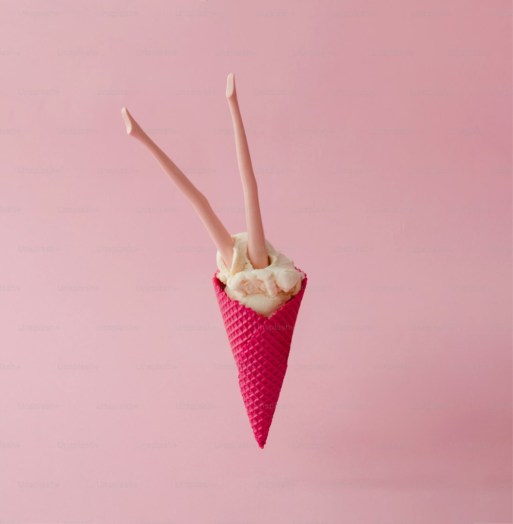 Gambe di bambola in gelato alla vaniglia con cono rosso su sfondo rosa pastello. Concetto estivo creativo.