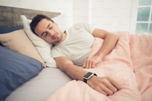 Young handsome man in bedroom lying on bed. Young man with smartwatch. Nice loft interior. Man sleeping