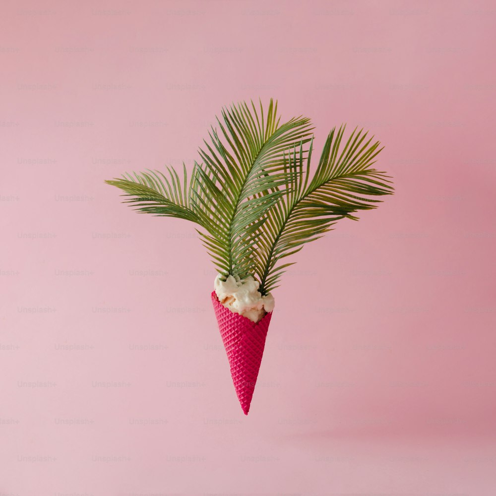 Palm tree leaves in vanilla ice cream with red cone on pink pastel background. Creative summer concept.