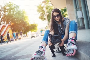Retrato urbano de una chica hermosa y atractiva con bulldog francés y gafas de sol. Colores cálidos del verano y neblina. Fuerte luz de fondo.