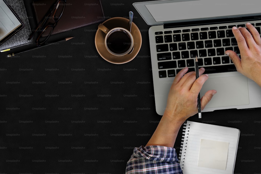 Man hand on laptop keyboard with blank screen monitor on dark surface leather table.