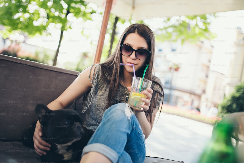 Bella ragazza seduta nel ristorante caffetteria con il suo adorabile cucciolo di bulldog francese. Tema persone e cani.