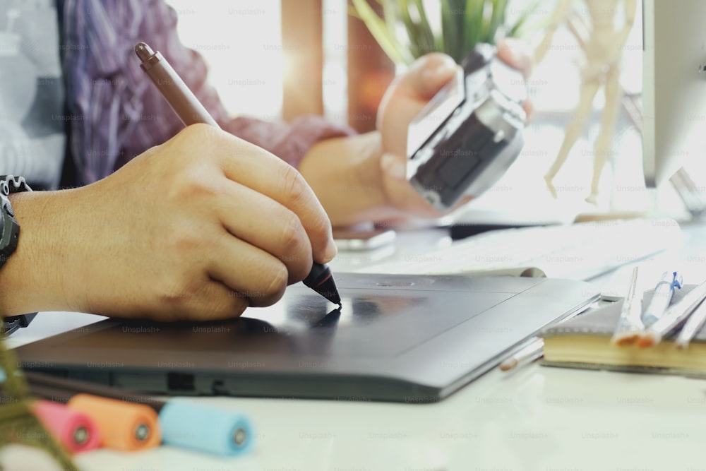 Young hipster graphic designer man using digital graphic tablet while working at modern office, professional male retoucher sitting at modern workspace with wooden table, generic design tablet