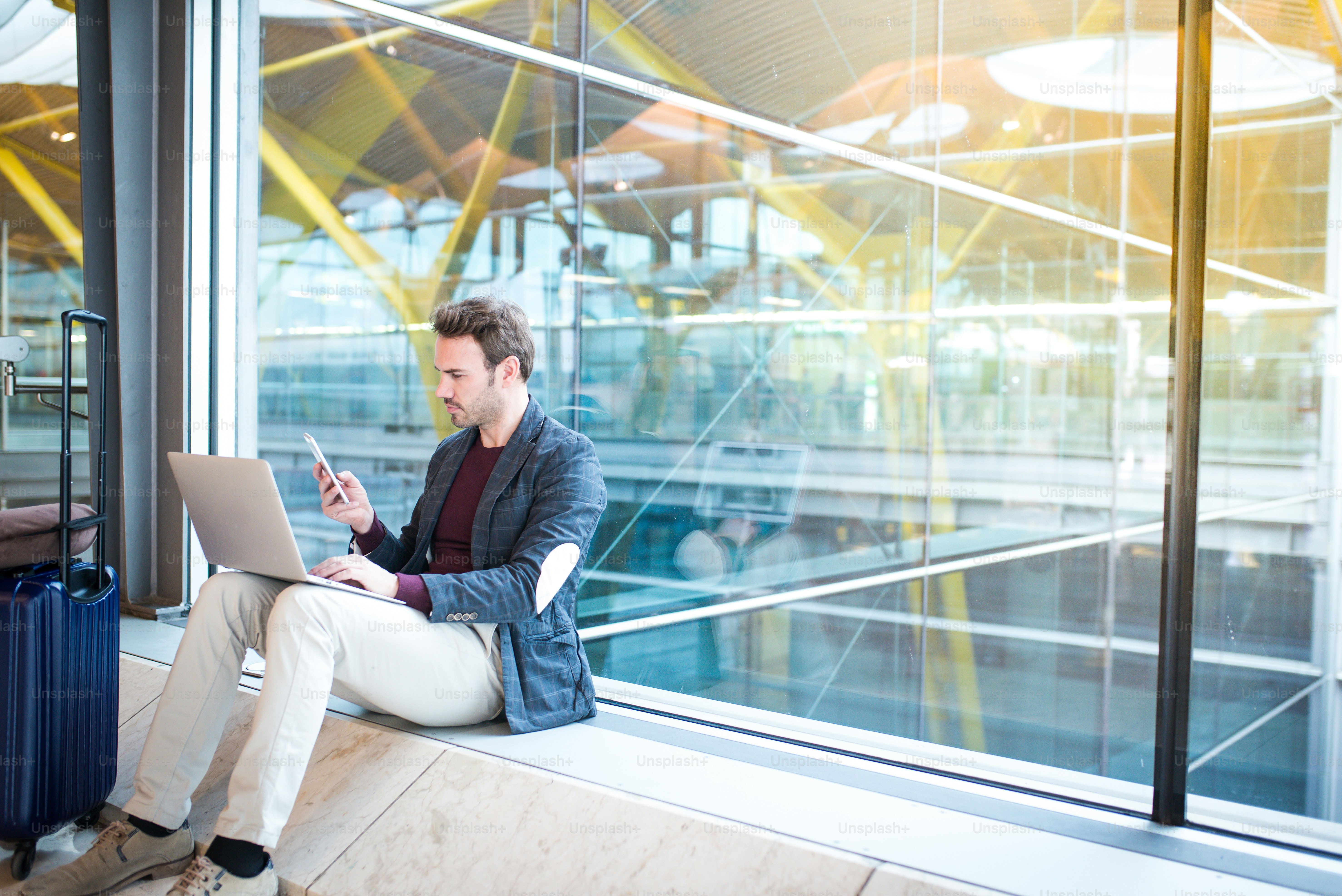 man sitting at the airport using laptop and mobile phone next to the window.