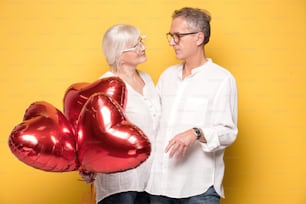 Beautiful happy senior couple posing together with red balloons, smiling.