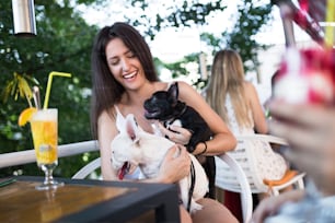 Beautiful young woman sitting in cafe with her adorable French bulldog puppy. Spring or summer city outdoors. People with dogs theme.