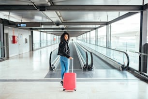 donna nera nel tapis roulant dell'aeroporto con una valigia rosa.