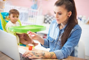 Mãe jovem alimentando seu bebê em home office