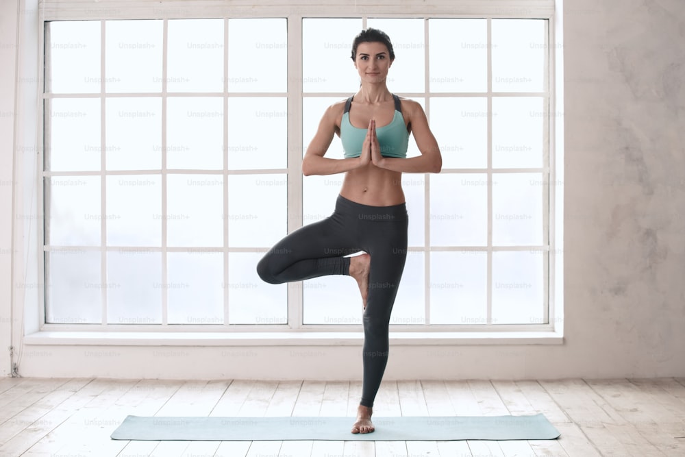 Junge Frau, die Yoga-Meditation Asana-Übung in Innenräumen in der Nähe des Fensters macht