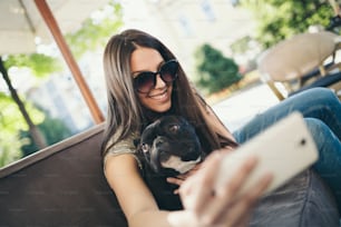 Hermosa adolescente sentada en un café restaurante con su adorable cachorro de bulldog francés. Tema de personas y perros.