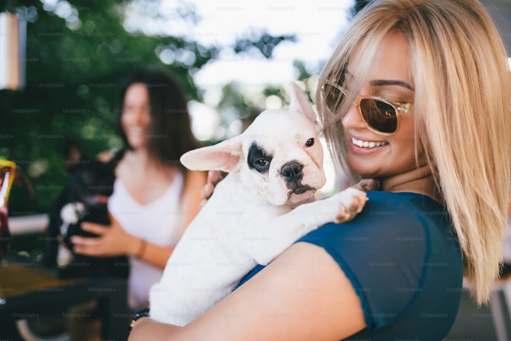 Beautiful young woman sitting in cafe with her adorable French bulldog puppy. Spring or summer city outdoors. People with dogs theme.