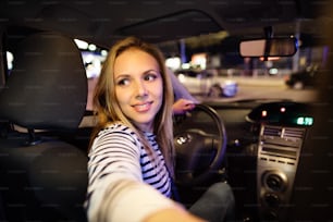 夜に彼女の近代的な車を運転する街の美しい若い女性。