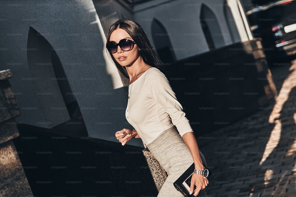 Attractive young woman carrying her smart phone and wallet while walking outdoors