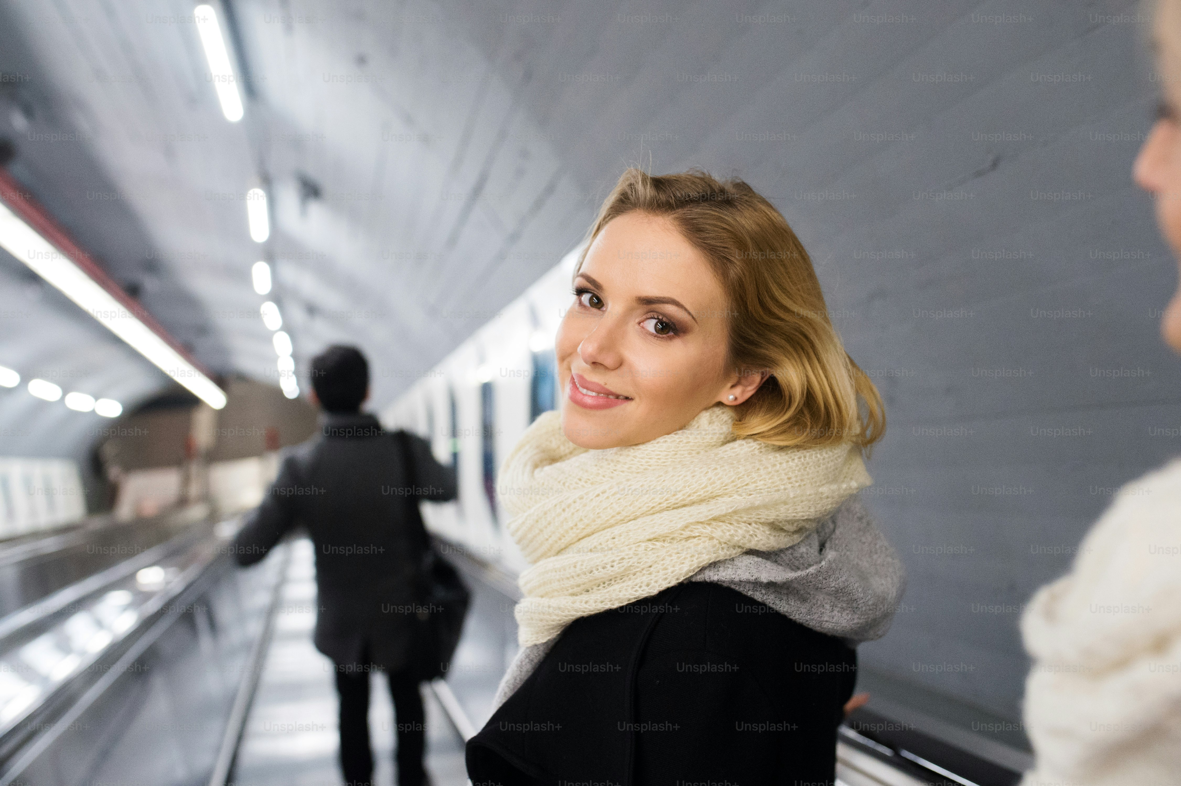 Beautiful young blonde woman in black coat and big woolen scarf standing at the escalator in Vienna subway