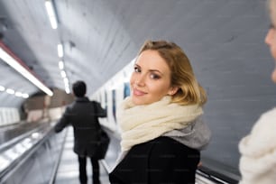 Mulher loira jovem bonita no casaco preto e lenço de lã grande em pé na escada rolante no metrô de Viena