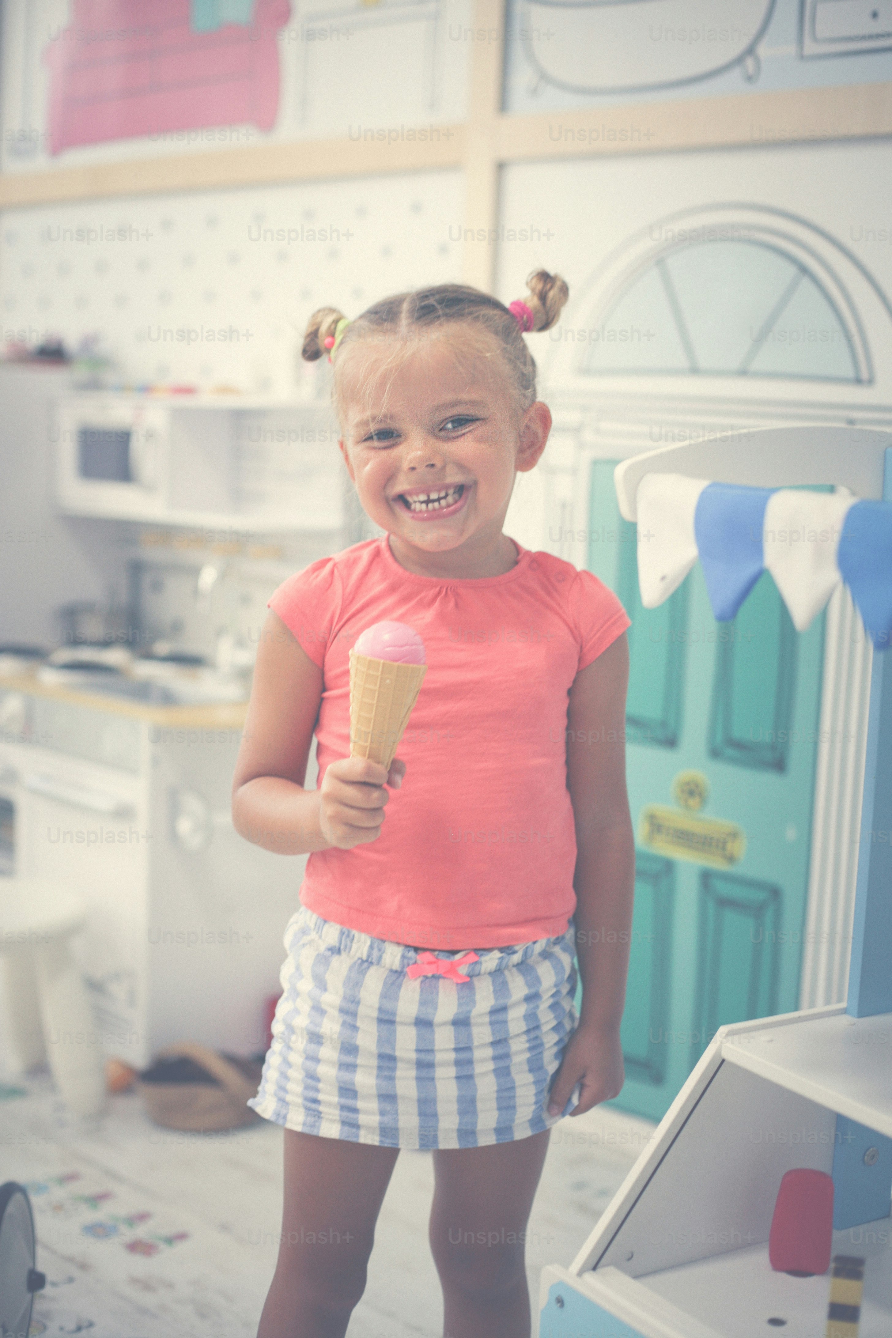 Little girl in playground. Girl standing in playroom and eating ace cream.