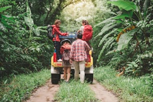 Happy asian young travellers with 4WD drive car off road in forest, young couple walking with backpacks and another two are enjoying on 4WD drive car. Young mixed race Asian woman and man.