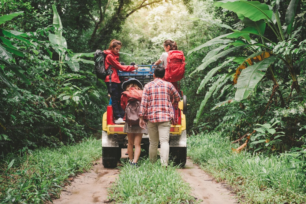Happy asian young travellers with 4WD drive car off road in forest, young couple walking with backpacks and another two are enjoying on 4WD drive car. Young mixed race Asian woman and man.