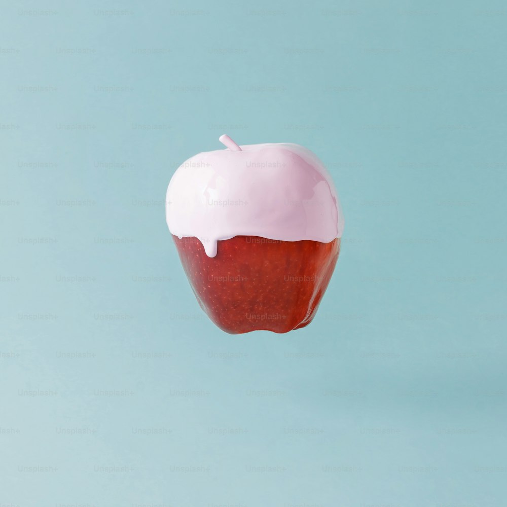 Roter Apfel mit Eiscreme-Topping auf pastellblauem Hintergrund. Kreatives Food-Konzept.