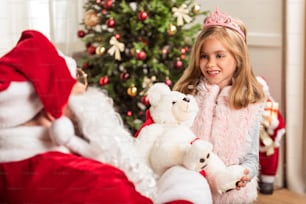 La princesita feliz está recibiendo un regalo de Santa Claus. Está de pie y sonríe agradecida. Retrato