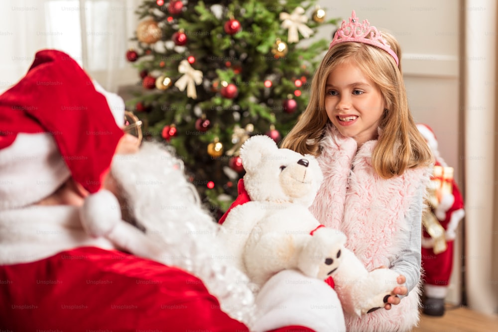 Happy little princess is getting gift from Santa Claus. She is standing and smiling gratefully. Portrait