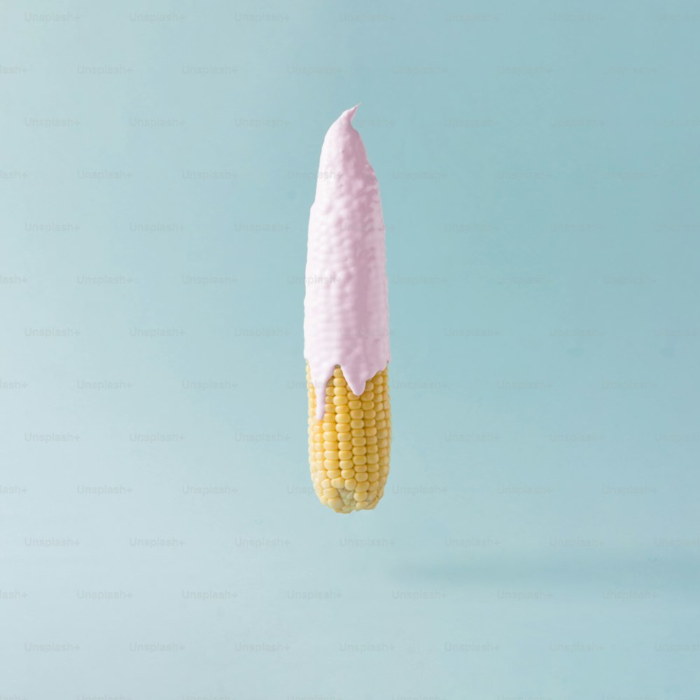 パステルブルーの背景にアイスクリームをトッピングしたトウモロコシの穂軸。フードクリエイティブのコンセプト。