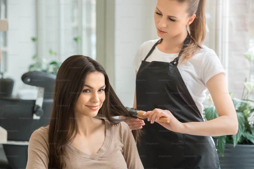 Young female sitting in hair salon hairdo styling brush