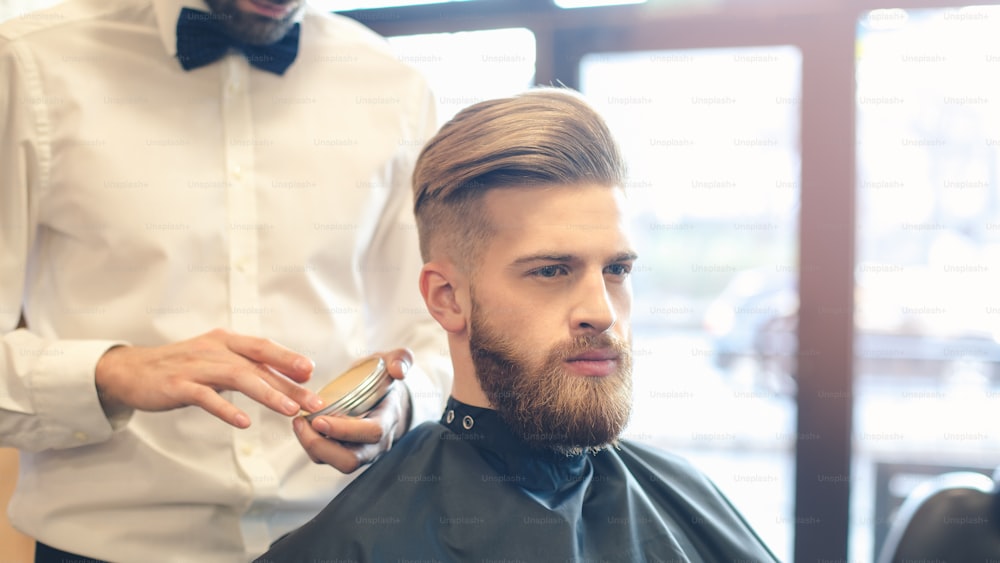 Young man sitting in a barbershop while barber finishing hairstyle