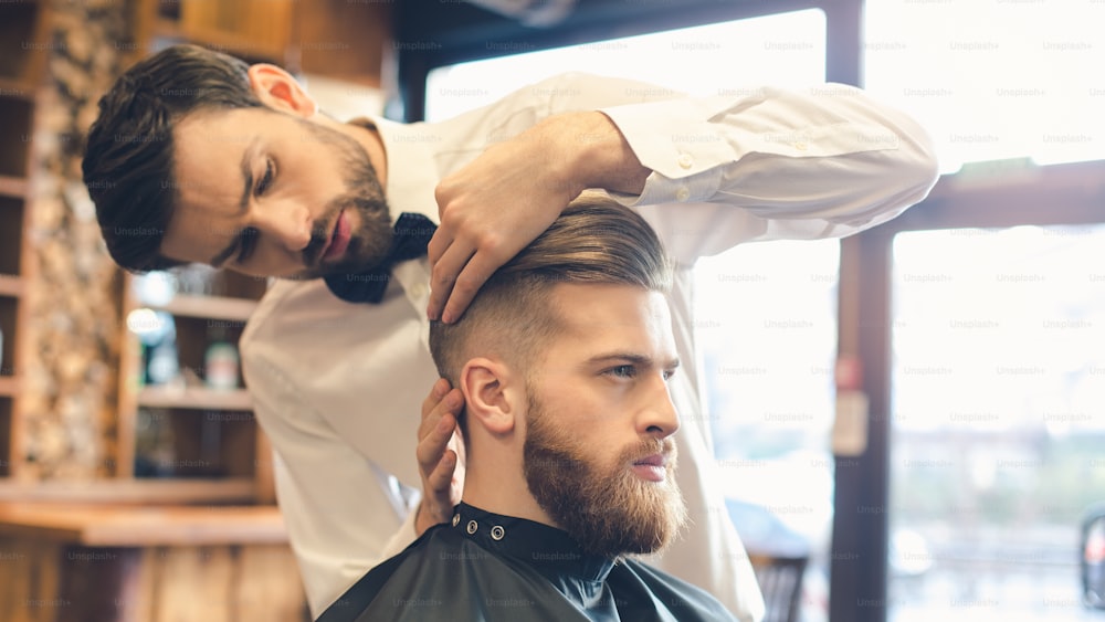 Junger Mann sitzt in einem Friseursalon, während der Friseur die Frisur beendet