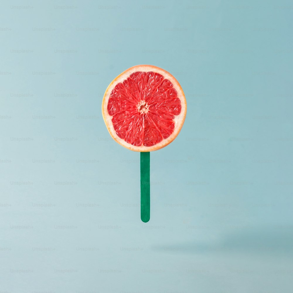 Rote Grapefruit mit Eisstange auf pastellblauem Hintergrund. Kreatives Food-Konzept.