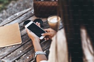 Vista trasera de una mujer joven sosteniendo un teléfono inteligente mientras está sentada en un restaurante al aire libre