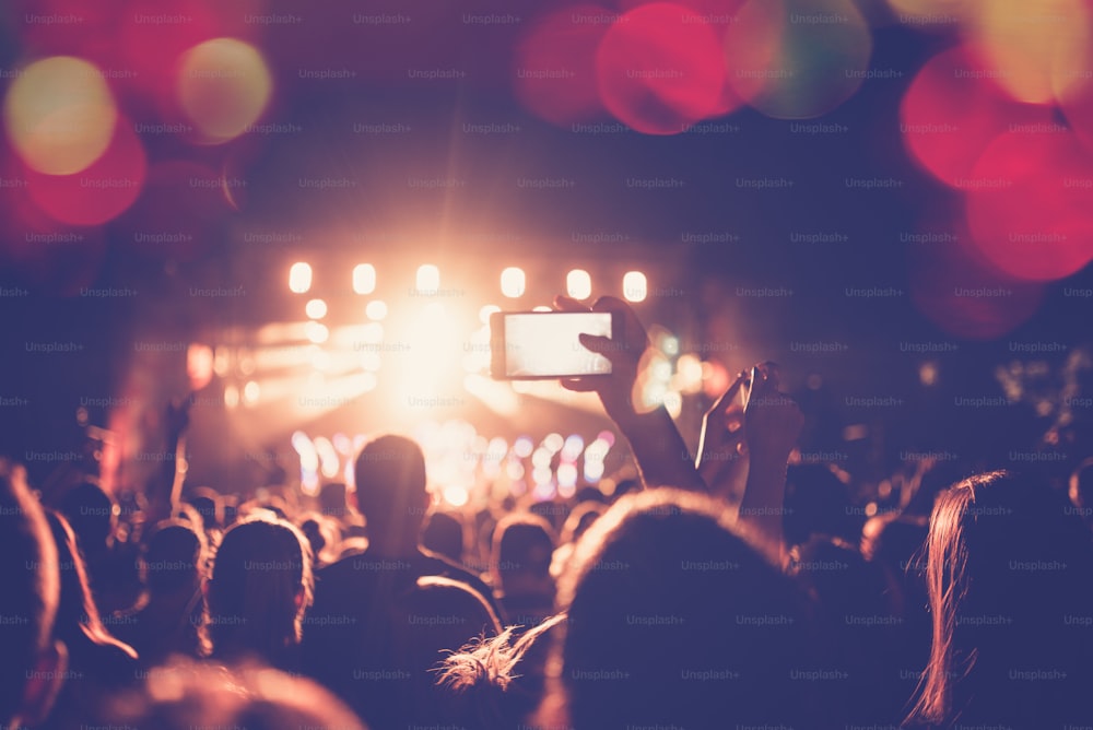 Silhouettes of festival concert crowd in front of bright stage lights. Unrecognizable people and colorful effects.