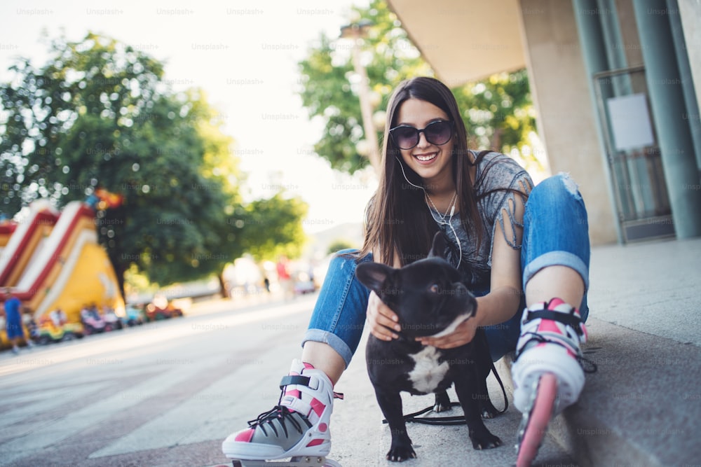 Retrato urbano da menina bonita e atraente com buldogue francês e óculos de sol. Cores quentes de verão e neblina. Luz de fundo forte.