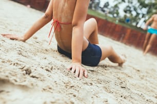 Young woman sitting on sand and resting while playing beach volleyball on beautiful sunny day.