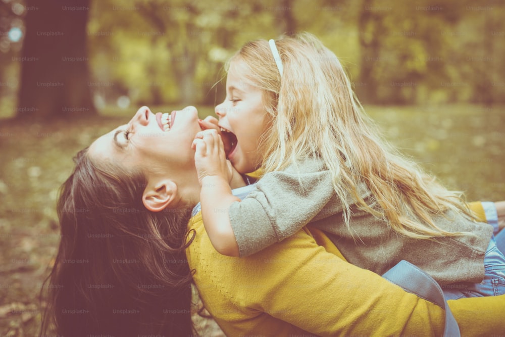 Mother and daughter outdoors in a meadow. Little girl sitting on mother lap and tick her mother.
