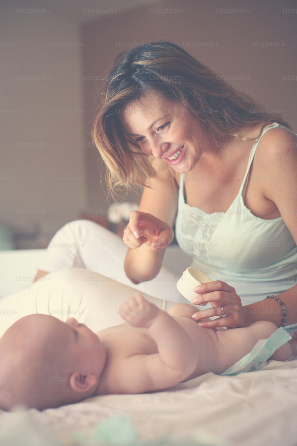 Mother changing diaper her little baby on the bed. Mother using baby cream.