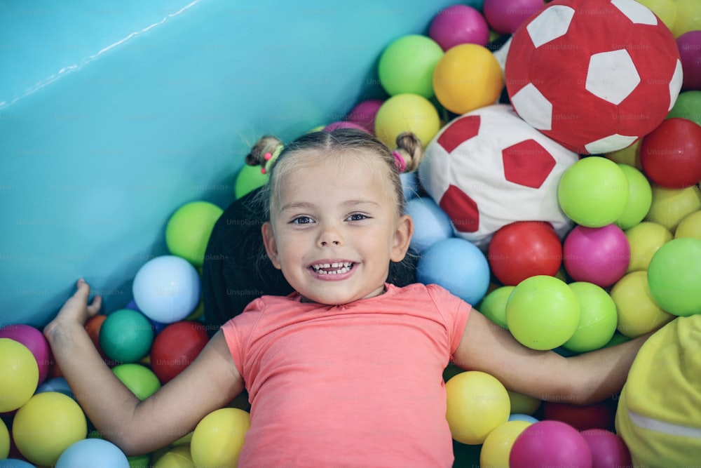 Caucasian girl lying on colored ball. Little girl playing in playground.