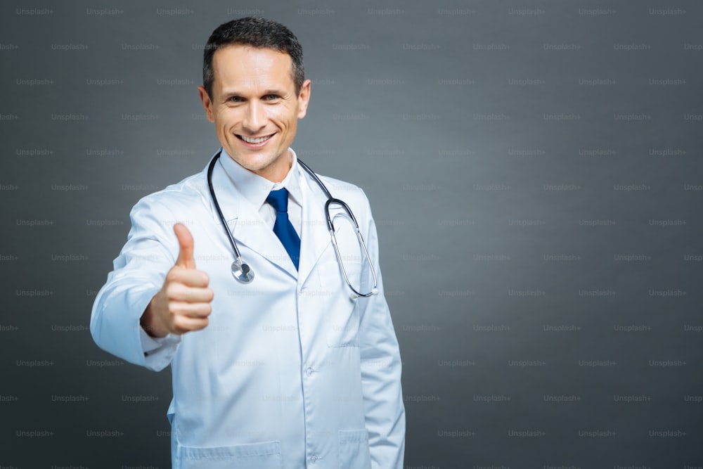Everything is cool. Waist up shot of a cheerful male doctor looking into the camera with a cheerful smile on his face while standing straight and showing a thumbs up sigh.