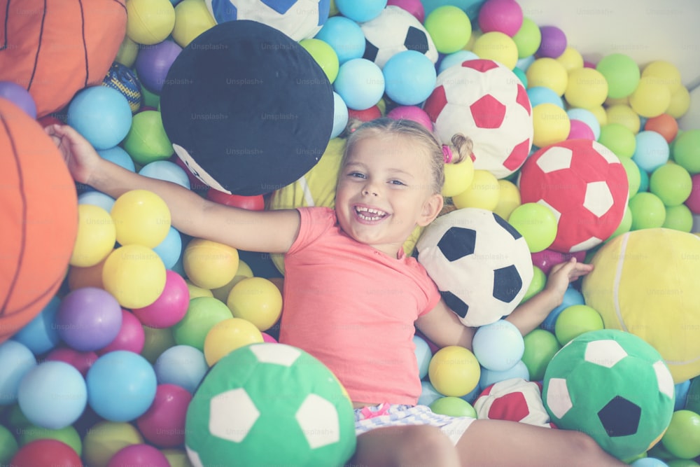 色付きのボールの上に横たわっている白人の女の子。遊び場で遊んでいる小さな女の子。