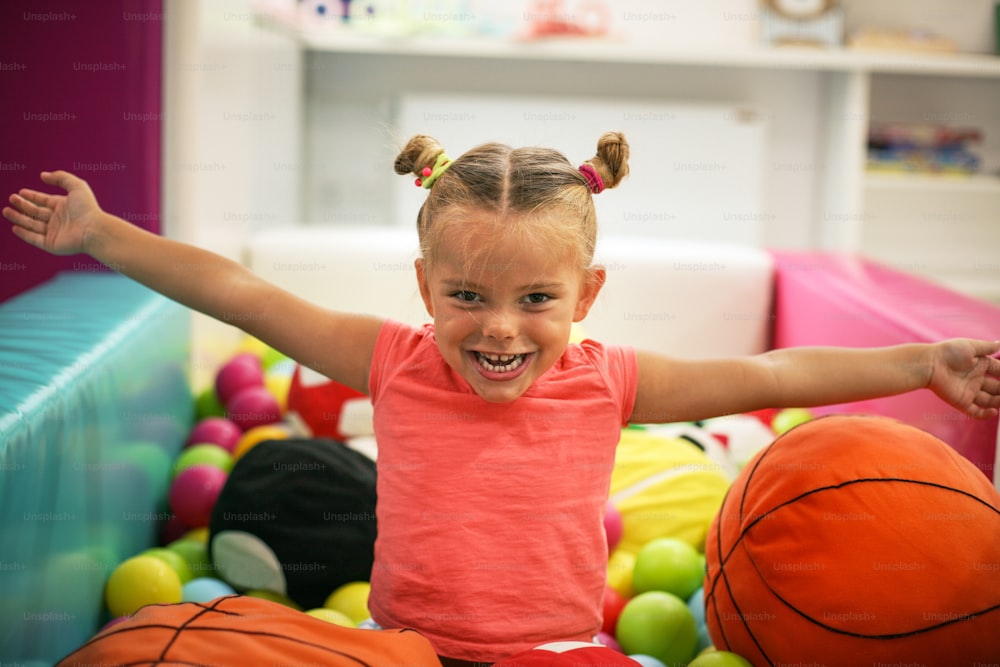Menina caucasiana com braços abertos sentada na bola colorida. Menina brincando no playground.
