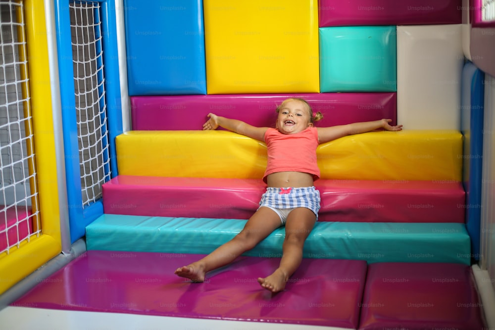 Ragazza caucasica nel parco giochi. Bambina sdraiata sulle scale di gomma con le braccia aperte". n