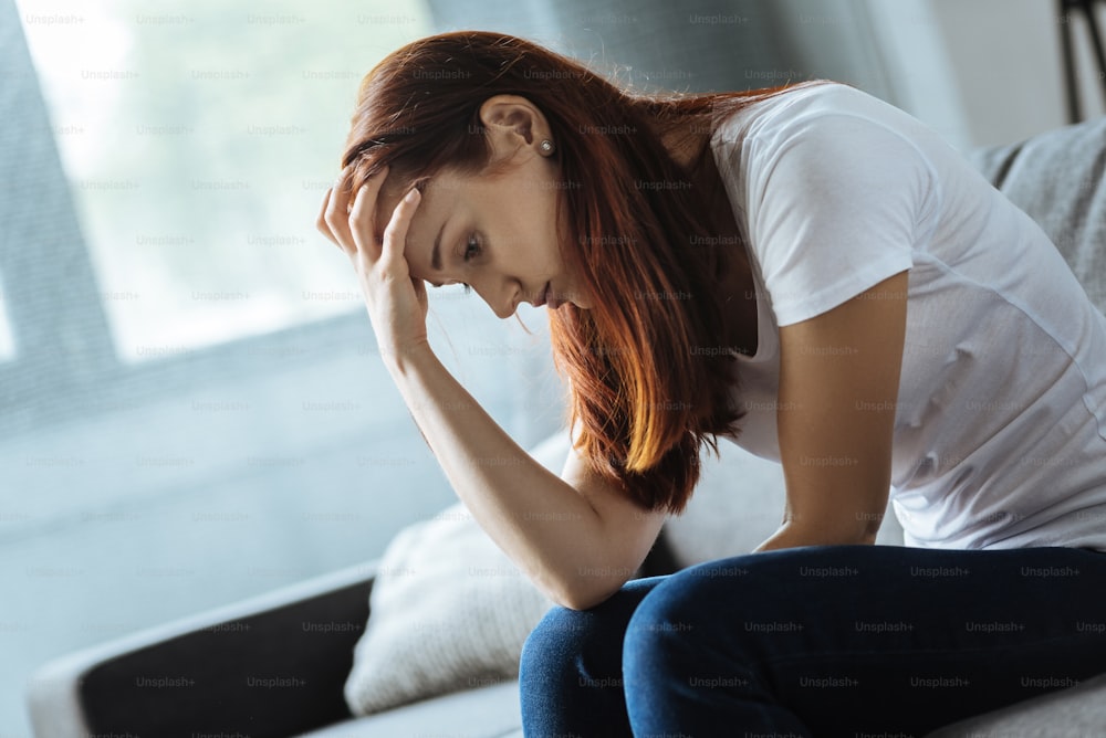 C’est un problème difficile. Femme malheureuse et sans joie, assise sur le canapé et se tenant le front tout en cherchant une solution à son problème