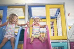 Zwei kleine Mädchen auf dem Spielplatz. Mädchen rutschen auf der Rodelbahn.