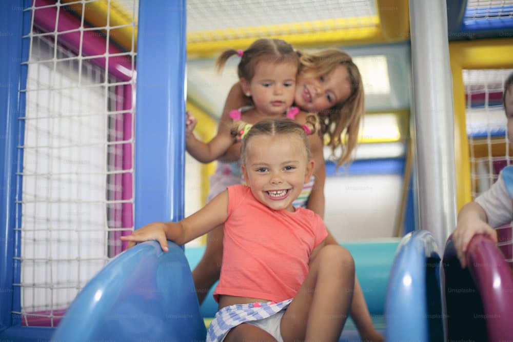 Three little girls in playground. Girls sliding on toboggan.