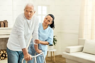協力的であること。彼女の高齢の患者の後ろに立ち、支えながら彼の手を握っている愉快で素敵なプロの介護者