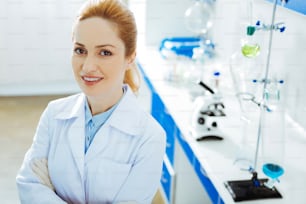 Joyful mood. Attractive female keeping smile on her face and looking straight at camera while standing in the laboratory